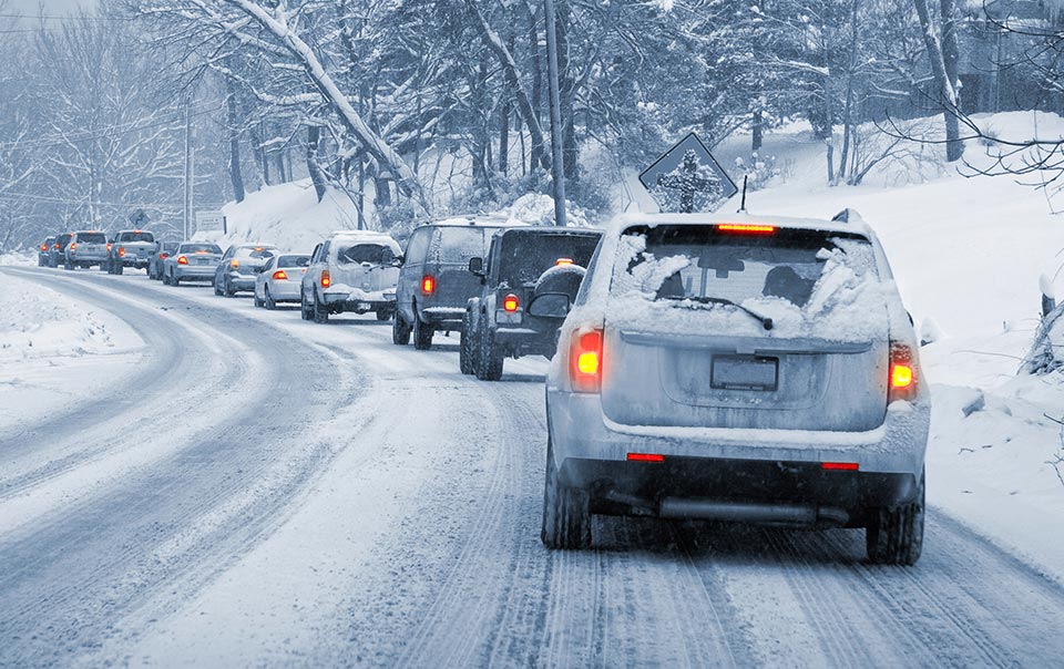 Long line of cars driving through a blizzard on a snowy road